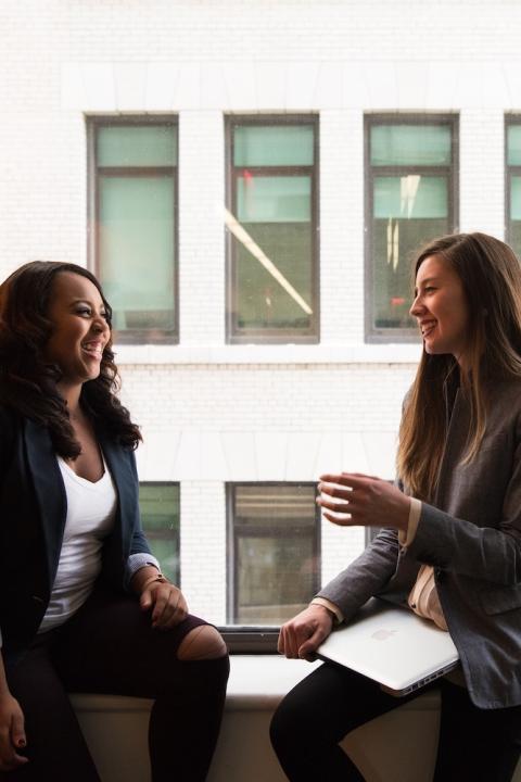 Two women sitting by a window talking. 