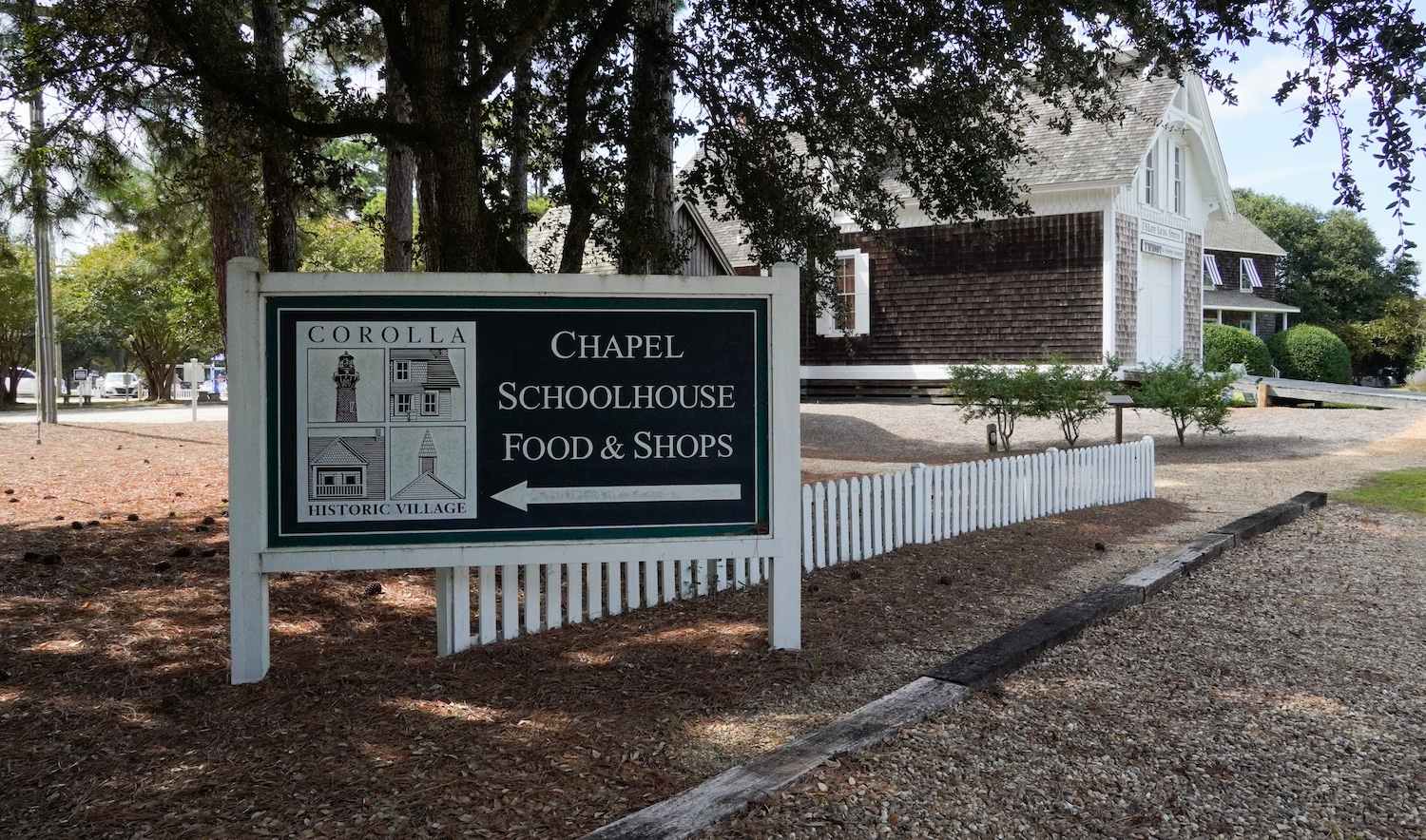 A sign welcoming visitor to the Corolla Historic Village, pointing them in the direction of the schoolhouse — employee housing