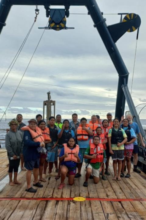 Residents of Mauke, Cook Islands, stand together on the deck of a deep-sea mining boat under a pulley system.