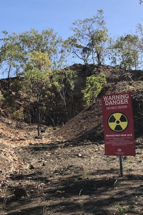 A danger warning sign sits in front of a mount of dirt a trees, designating an abandoned mining site in Australia.