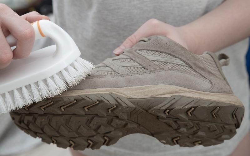 cleaning lightweight slip on work shoe with white brush in right hand and shoe in left hand